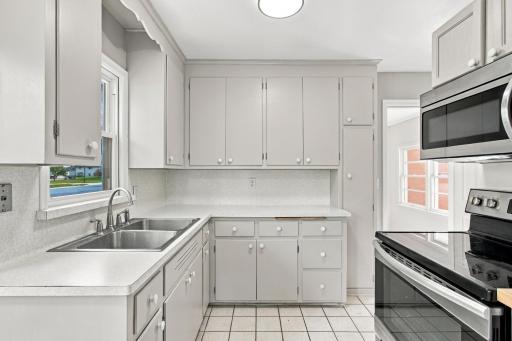 Kitchen. Double basin stainless sink under the window, deep upper cabinetry, and a stainless range with over-the-range microwave.