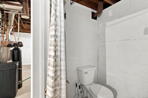 Lower level bath. Toilet and curtained enclosure adjacent to the water heater and water softener.