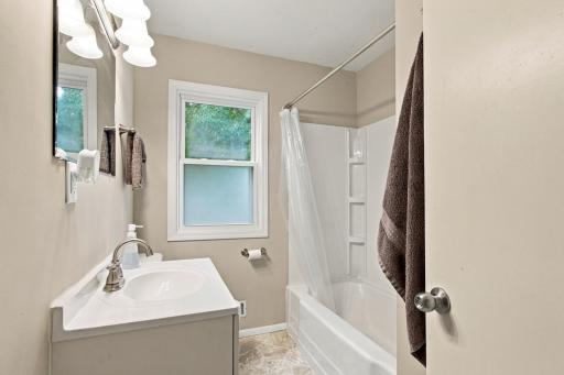 Main floor full bath. Vanity, tub and shower combination, window, and a multi-light vanity fixture.