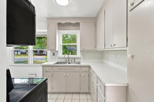 Kitchen. Painted cabinetry with a scalloped valance over the double window, light speckled countertops, and a stainless steel range with hood.