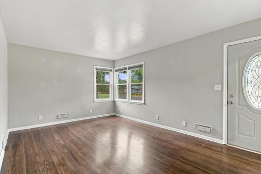 Living room. Hardwood flooring, corner windows, and a front entry door with an oval glass insert.