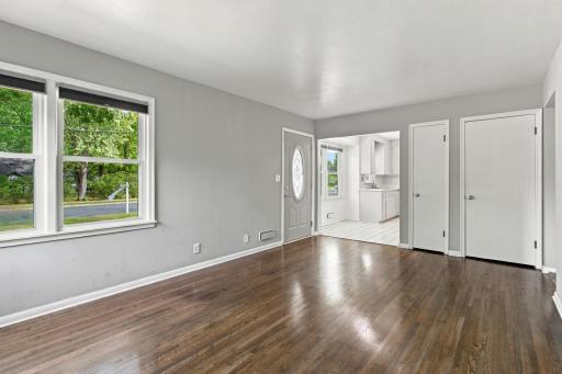 Living room. Hardwood flooring, a large front window, and open sightlines to the entry and kitchen.
