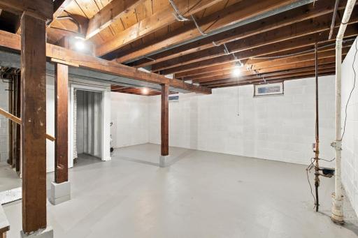 Lower level. Open unfinished space for storage or future finishing, with painted block walls and support posts.
