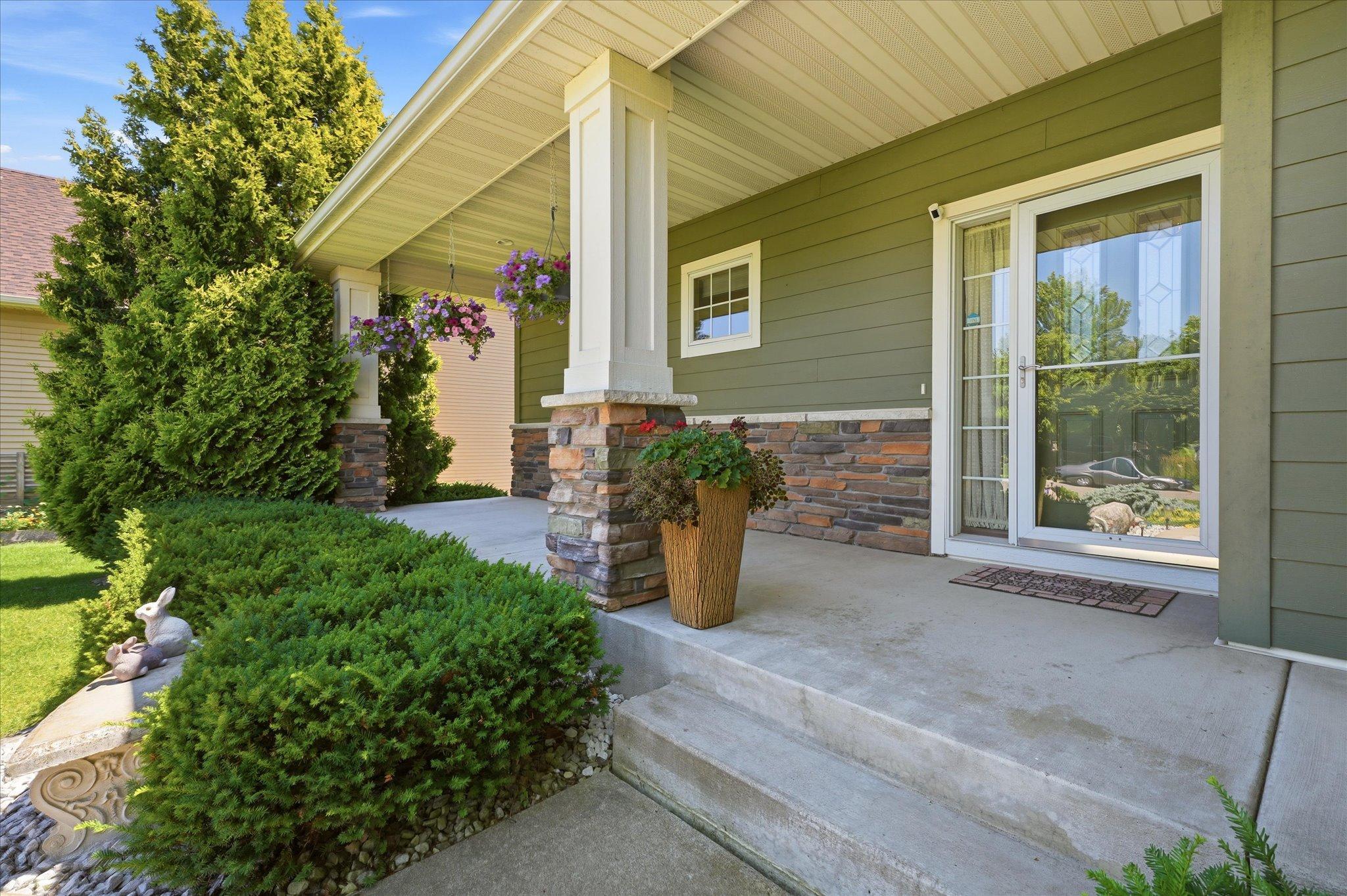 Inviting covered front porch provides the perfect place to relax and enjoy the neighborhood, highlighted by stone pillars, low-maintenance landscaping, and a decorative glass front entry door.