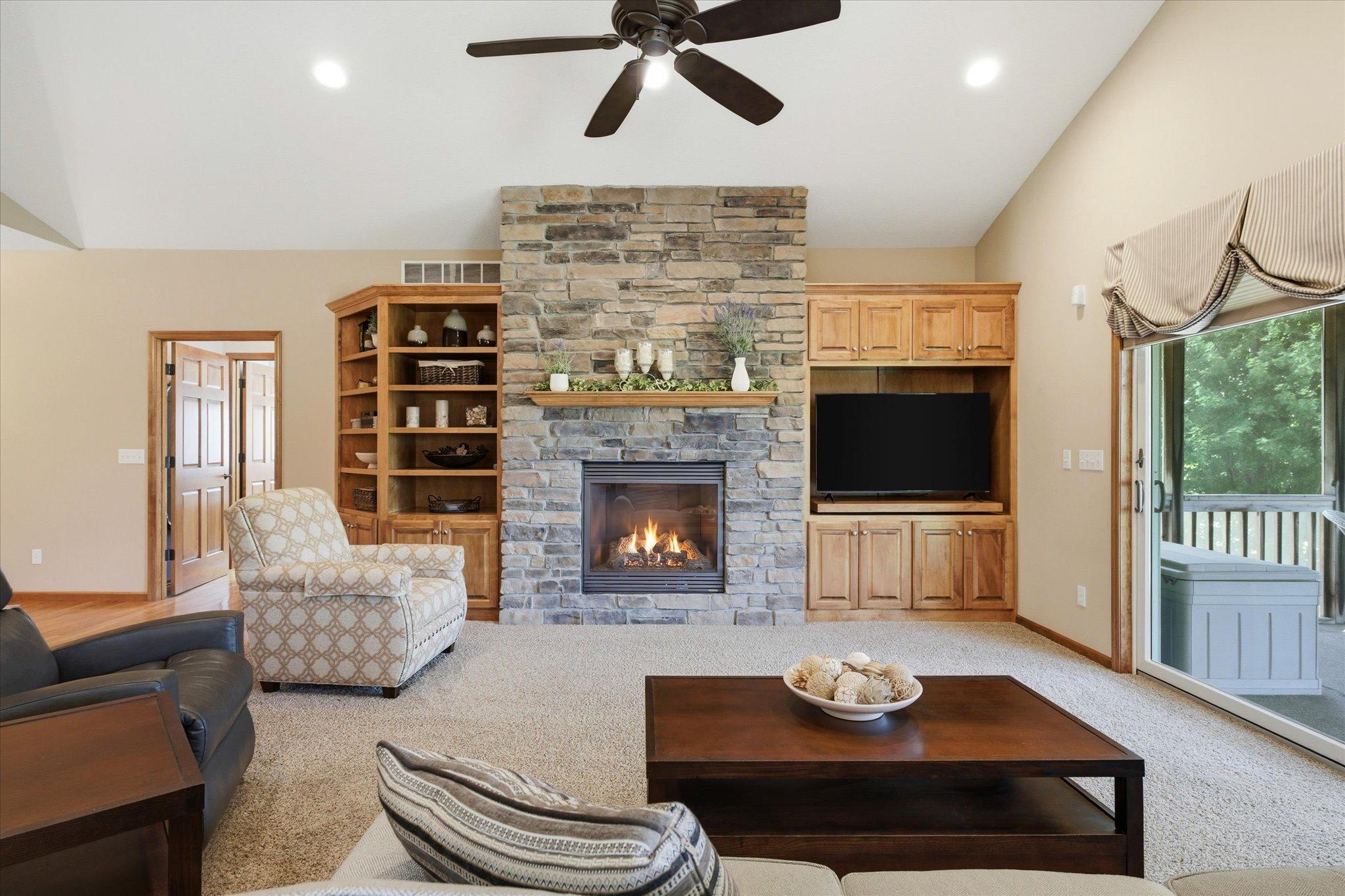 Stunning floor-to-ceiling stone gas fireplace serves as the centerpiece of the great room, complemented by custom-built maple cabinetry, built-in shelving, and large sliding glass doors leading to the three-season porch.