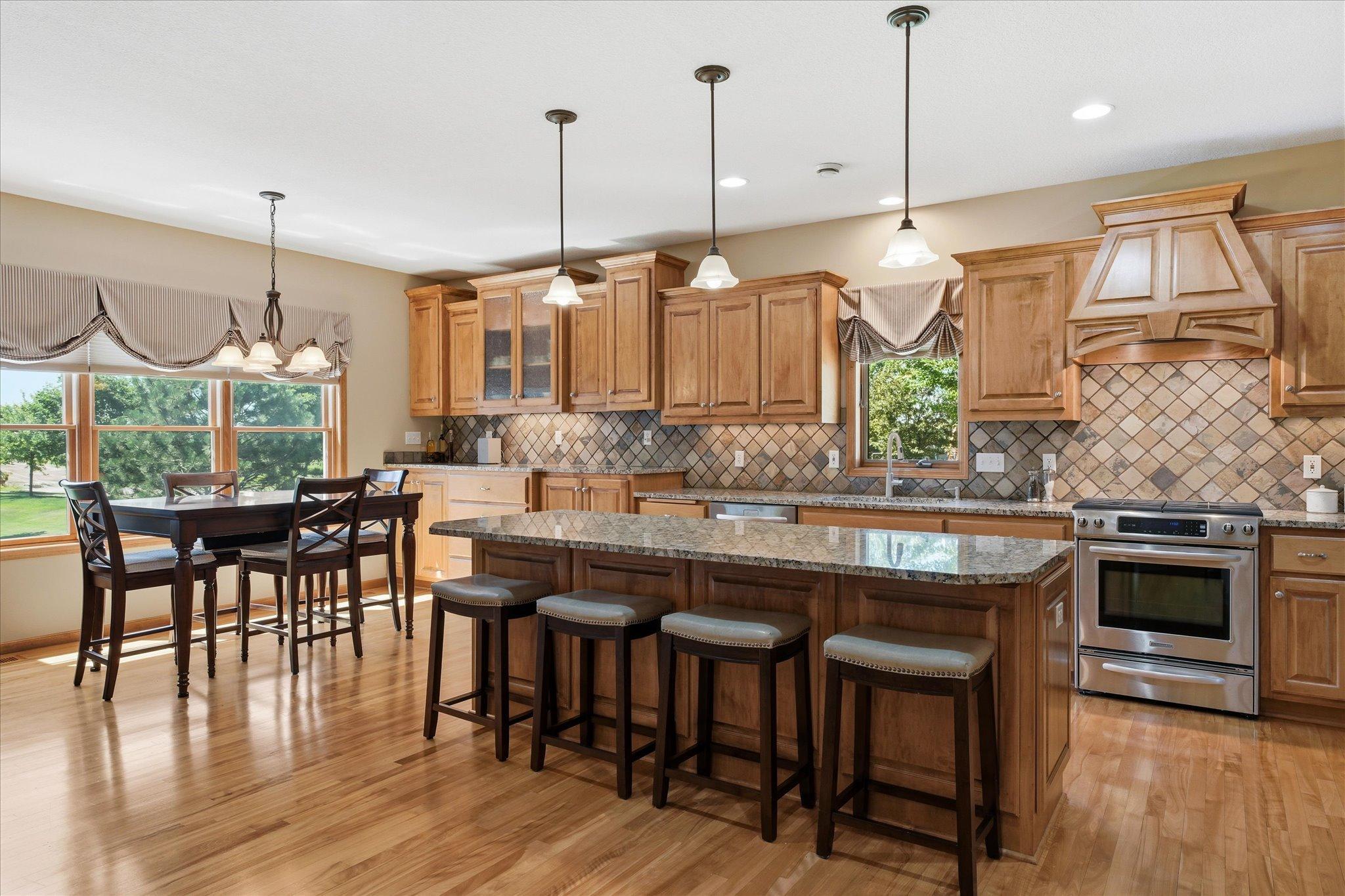 Beautiful chef's kitchen showcases custom maple cabinetry, granite countertops, a large center island with seating, under-cabinet lighting, and an adjacent dining area filled with natural light.