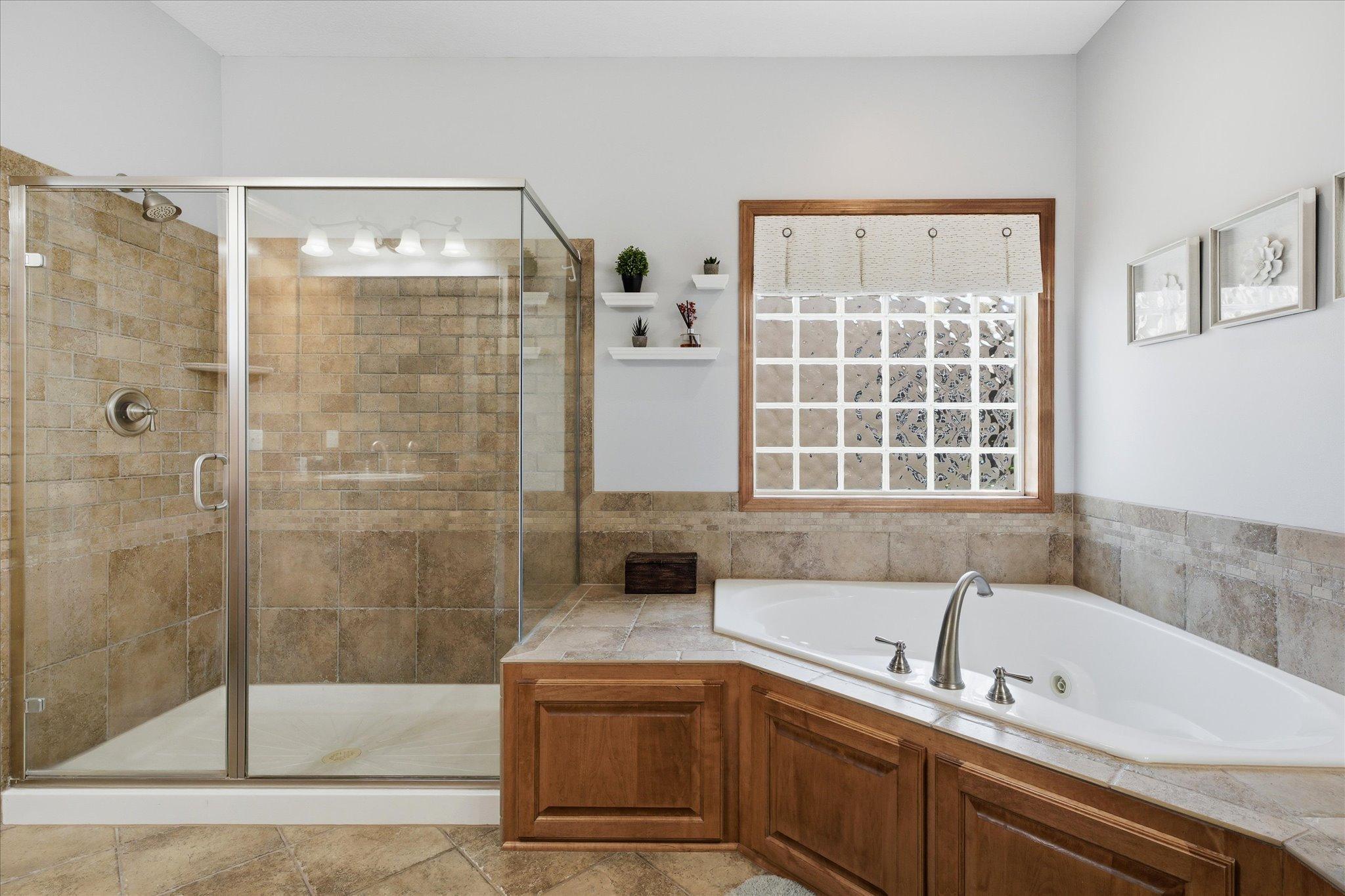Spa-inspired primary bath features heated tile floors, a large walk-in tiled shower with glass enclosure, relaxing corner jetted soaking tub, and beautiful glass block window that fills the space with light while maintaining privacy.