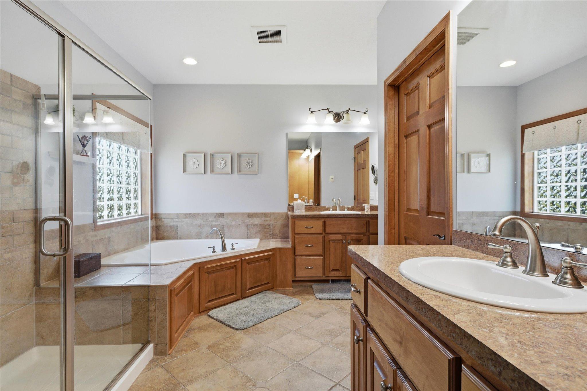 Enjoy the convenience of two separate 42-inch comfort-height vanities, heated floors, a large walk-in shower with glass doors, corner jetted tub, and abundant natural light from the decorative glass block window.