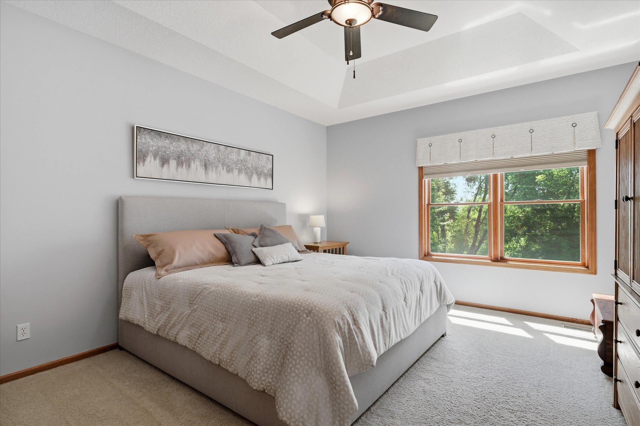 Spacious main floor primary suite offers a peaceful retreat with a dramatic pan-vaulted ceiling, plush carpeting, abundant natural light, and plenty of room for a king-sized bedroom set.