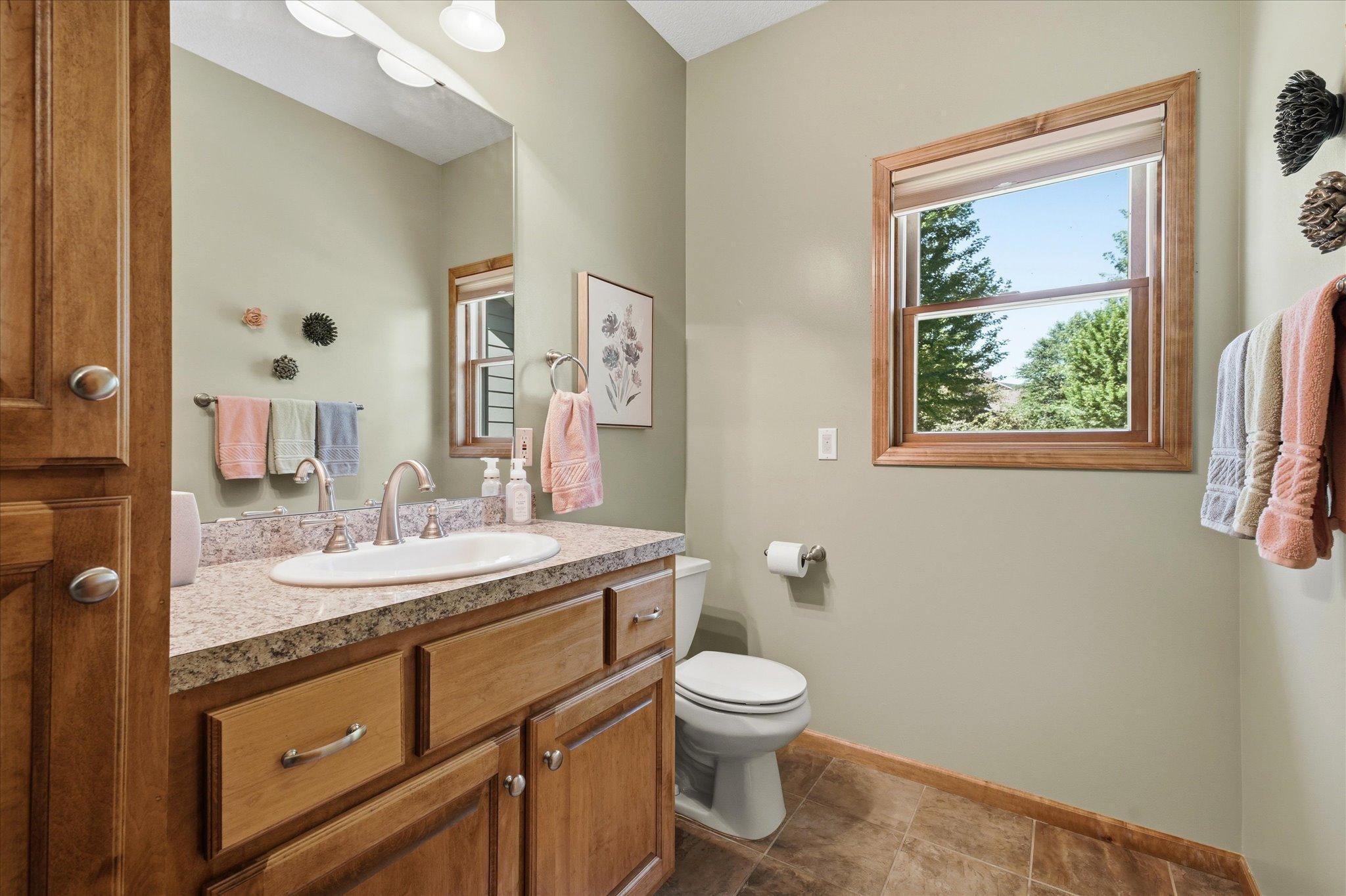 Convenient main-level powder room features a large vanity with ample storage, easy-care tile flooring, and a window that fills the space with natural light, perfect for guests and everyday convenience.