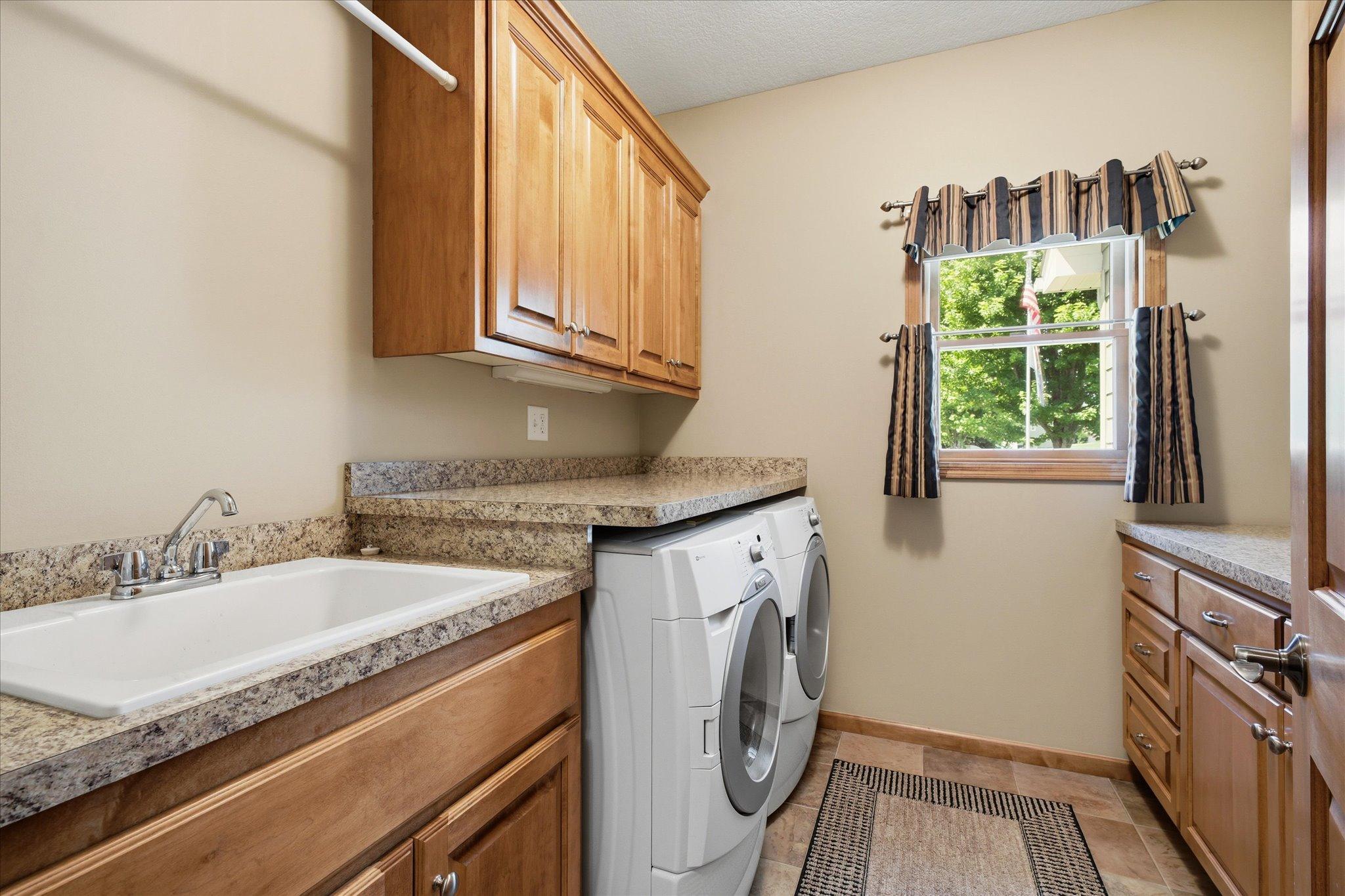 Convenient main-floor laundry room is designed for functionality with abundant cabinetry, generous countertop workspace for folding, utility sink, and plenty of storage to keep everyday tasks organized.
