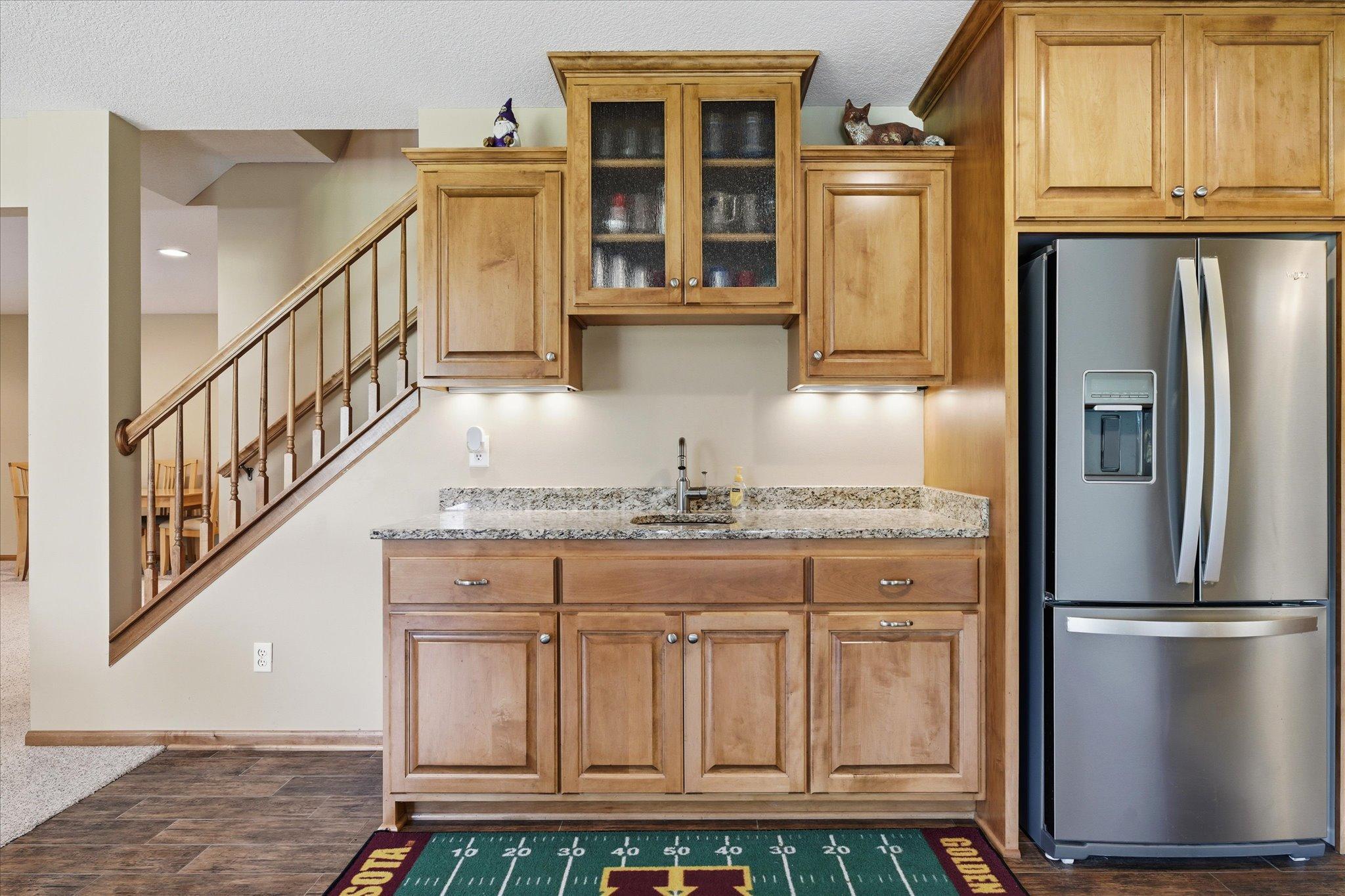 Custom wet bar features beautiful cabinetry, granite countertops, glass-front upper cabinets, a sink, and a full-size refrigerator, perfect for entertaining.