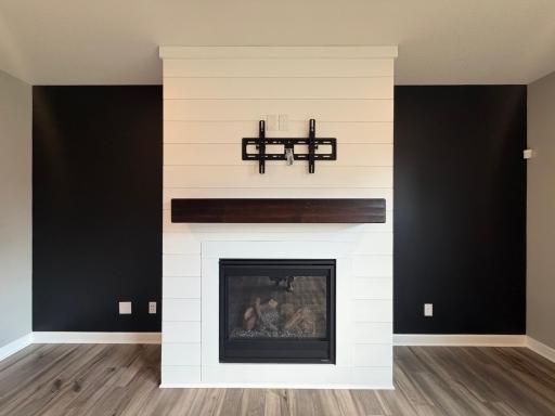 Actual photo of the home with the staging removed. The accent wall paint is a dark green & will remain dark green. The shiplap fireplace and large gas burning frame w/a log display is a show stopping feature! The TV mount is included.