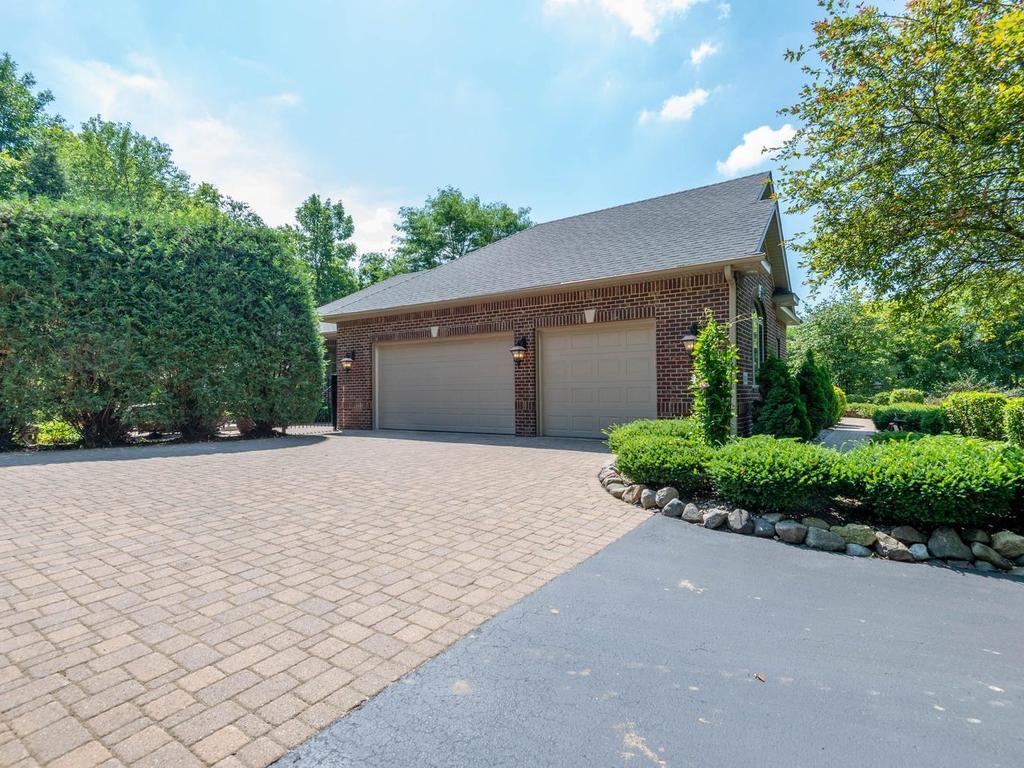 Heated 3-stall garage offers 946 sq ft, extra-high 135-inch ceilings with potential to accommodate a car hoist (not included), and a wide paver parking area framed by mature landscaping.