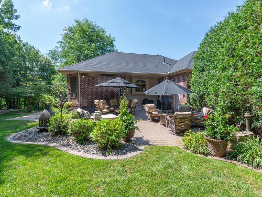 Another view of the expansive paver patio highlights multiple seating areas, mature landscaping, and a seamless connection to the covered grilling space.