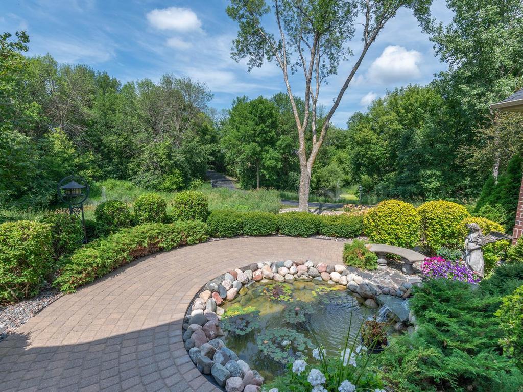 Curved paver walkway wraps around the decorative pond and landscaped gardens, with a fountain visible in the distance.