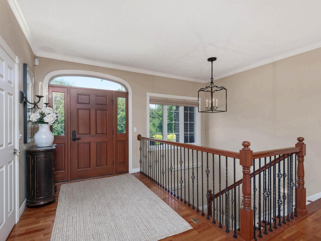 Welcoming foyer features a wood front door with sidelights and arched transom, hardwood flooring, crown molding, and an open staircase to the walkout lower level.