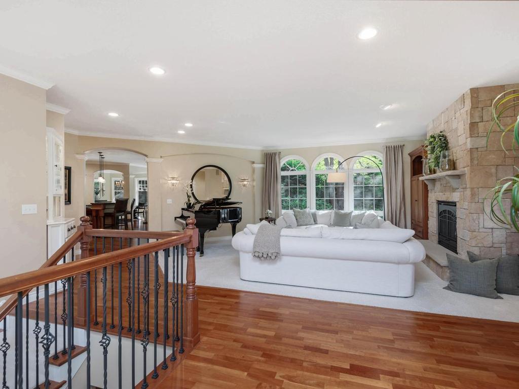 Inviting great room features a striking stone gas fireplace, arched windows framing wooded views, recessed lighting, and an open connection to the kitchen.