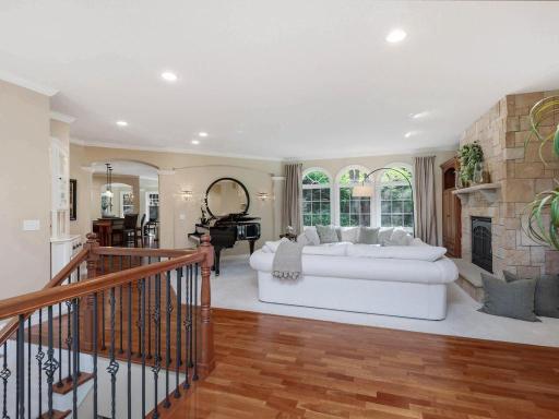Inviting great room features a striking stone gas fireplace, arched windows framing wooded views, recessed lighting, and an open connection to the kitchen.