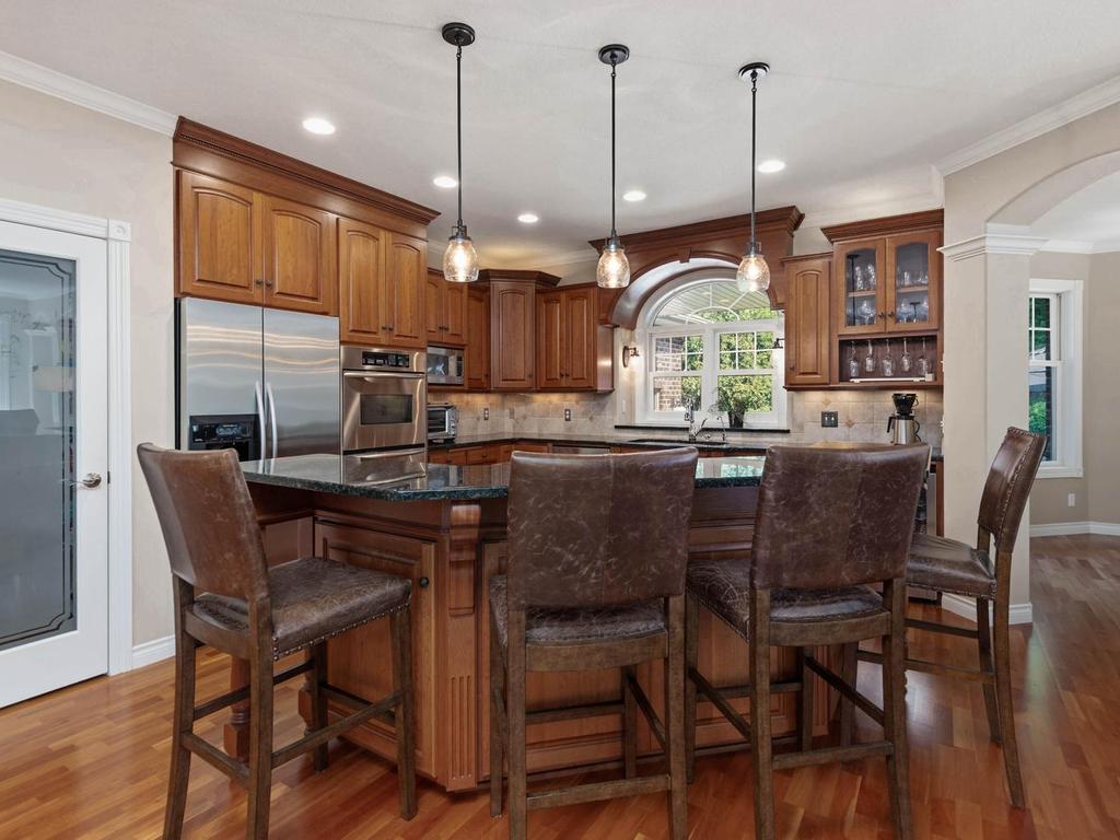Showstopping kitchen features rich cherry cabinetry, granite countertops, SS appliances, ctr island w/breakfast bar seating, pendant and recessed lighting, arched window above the sink, glass-front display cabinetry, double ovens, and walk-in pantry.