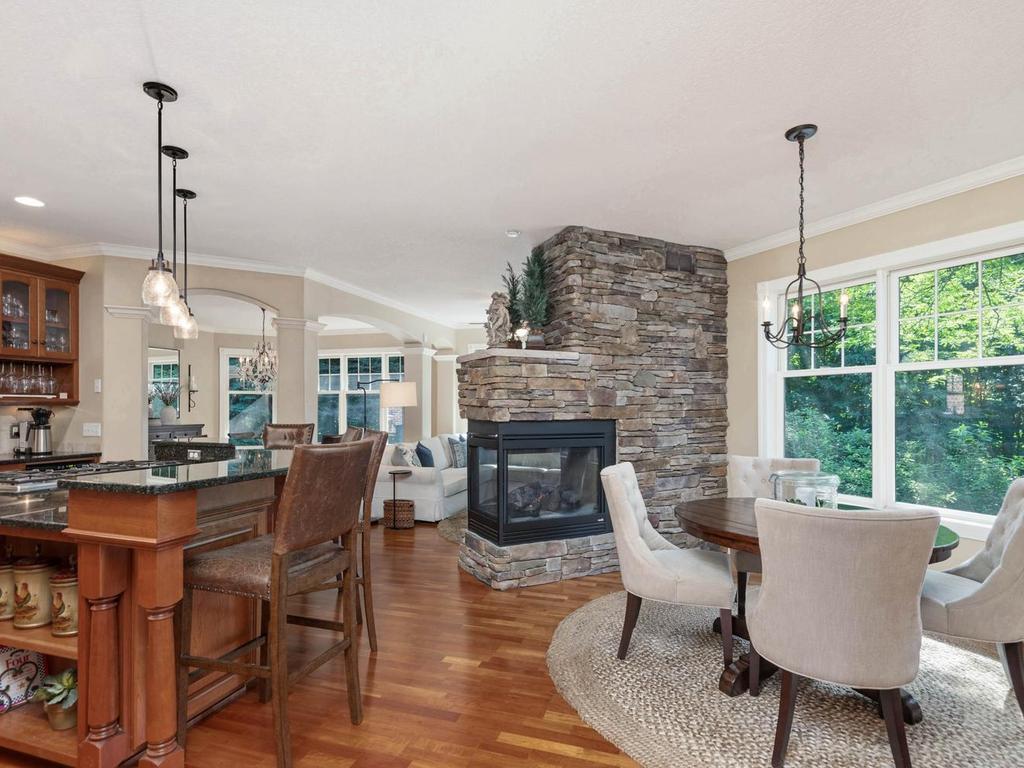 Open layout connects the kitchen, informal dining area, and hearth room around the 3-sided stone gas fireplace, creating an inviting space for everyday living and entertaining.