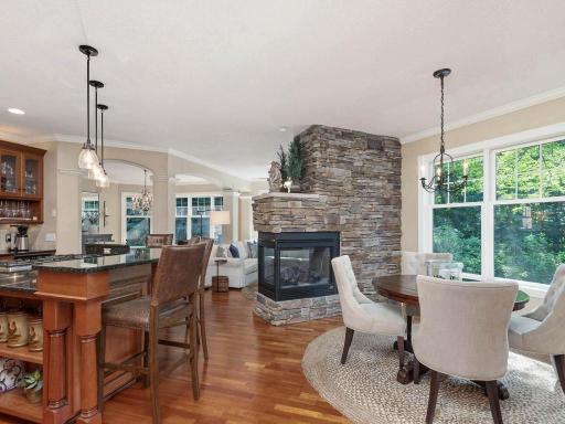 Open layout connects the kitchen, informal dining area, and hearth room around the 3-sided stone gas fireplace, creating an inviting space for everyday living and entertaining.