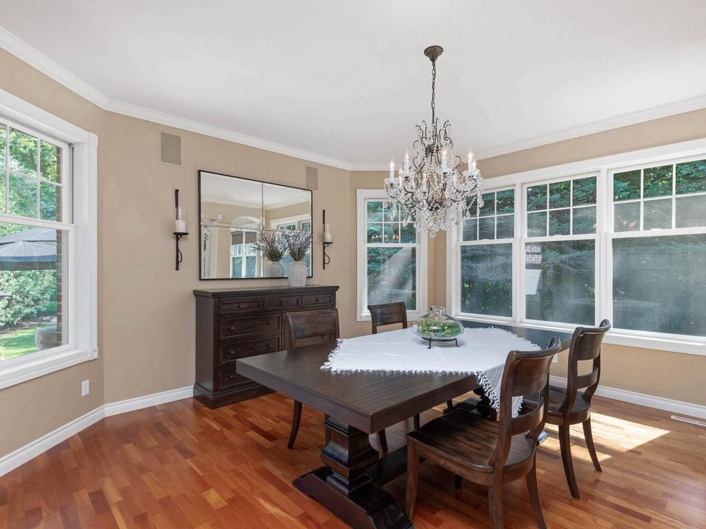 Formal dining room features hardwood flooring, crown molding, an elegant chandelier, and walls of windows overlooking the wooded backyard and outdoor living areas.