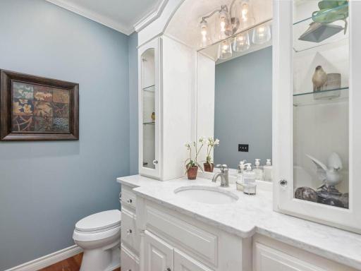 Main level Half Bath features a built-in glass display cabinetry, crown molding, and hardwood flooring.