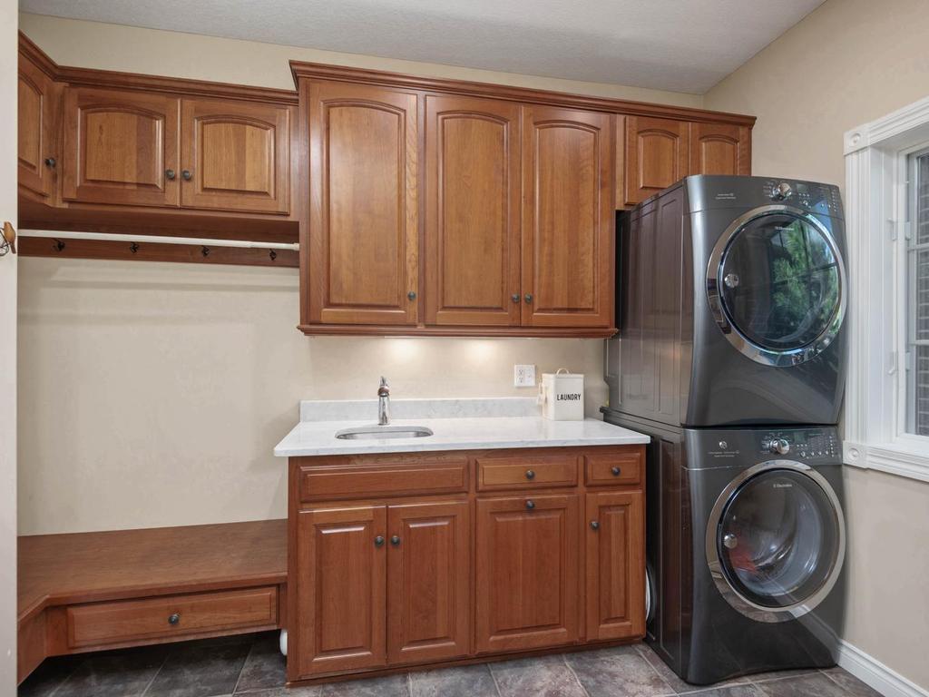 Main level laundry room offers abundant cherry cabinetry, utility sink, built-in bench and storage, stacked washer/dryer, and a window for natural light.