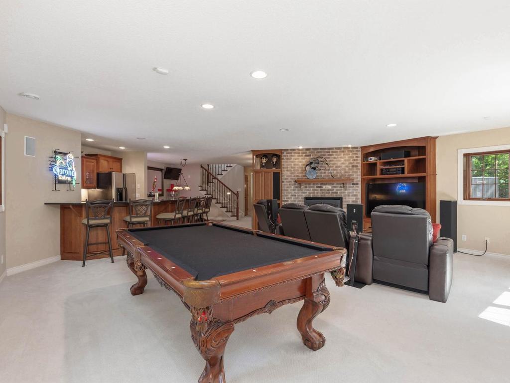 Expansive walkout lower level family room offers a stone gas fireplace, built-in entertainment center, wet bar, recessed lighting, and flexible space for movies, games, and gathering.