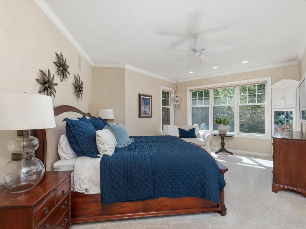 Spacious main level primary suite features crown molding, recessed lighting, ceiling fan, and a wall of windows overlooking the wooded setting.