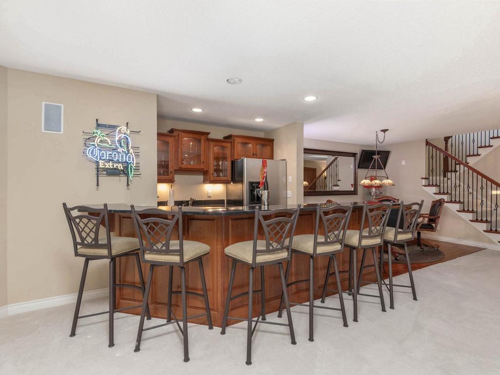 Lower level wet bar offers granite countertops, abundant cherry cabinetry, glass-front display cabinets, full-size refrigerator, sink, and generous bar seating overlooking the entertainment area.