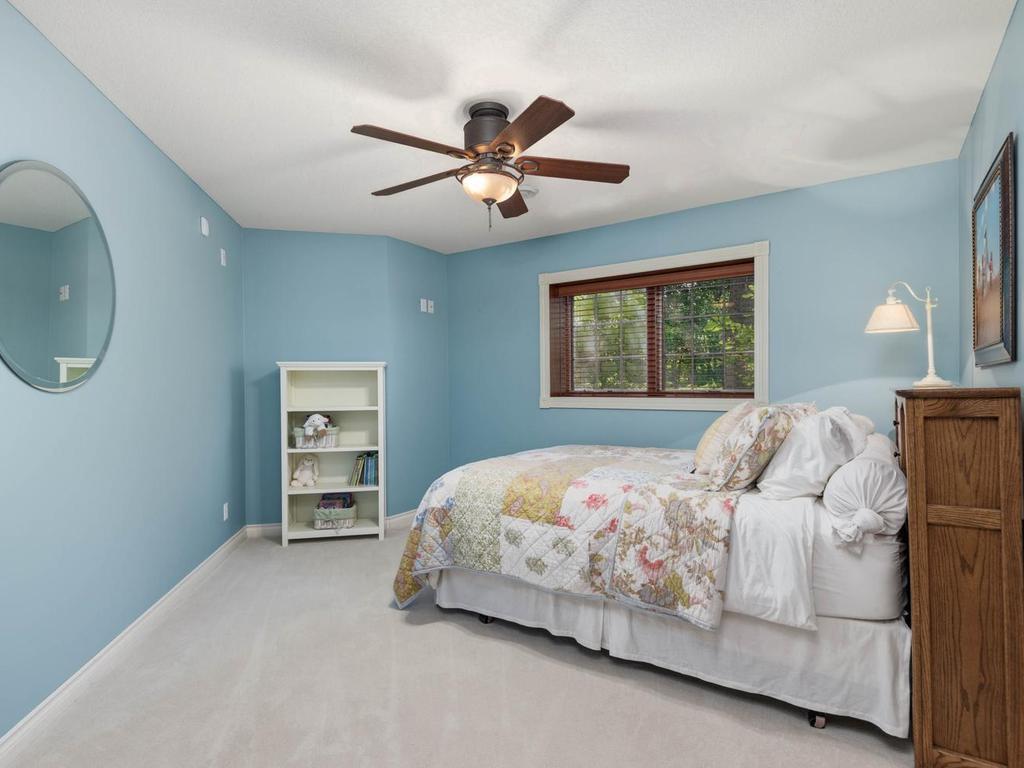 Lower level Bedroom 3 features a ceiling fan, neutral carpeting, and a window overlooking the wooded setting.