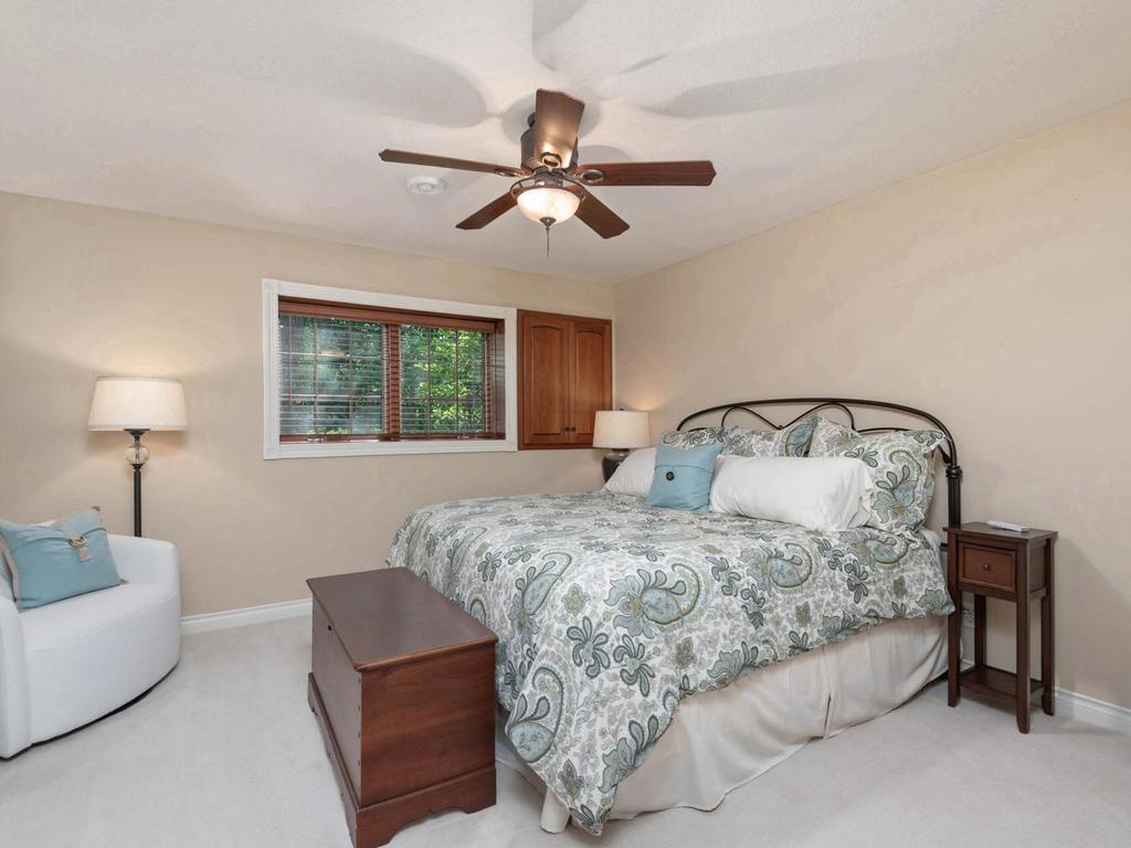 Lower level Bedroom 2 features a ceiling fan, built-in storage, neutral finishes, and a window overlooking the wooded setting.