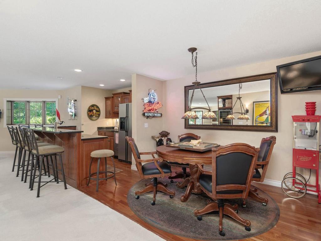 Additional view of the lower level entertainment area highlights the wet bar, game-table space, hardwood flooring, and open layout designed for gathering.