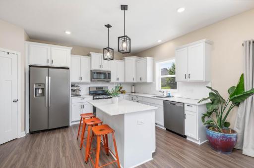 The white center island kitchen features staggered height cabinetry, tile backsplash, matching stainless appliances including a five burner gas stove, and quartz counter tops.