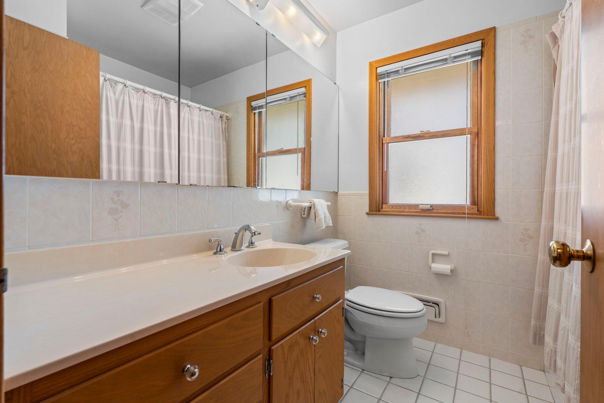 A centrally located full bathroom offers tile flooring, a tiled tub/shower, and vanity for added organization.