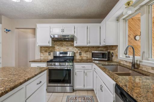 Updated kitchen with stainless appliances, granite counters, tile backsplash, and tile floors