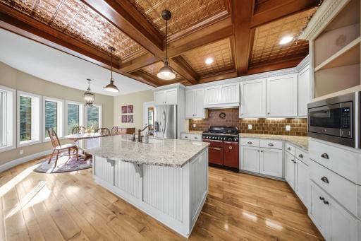 The gourmet kitchen impresses with a striking wood-accent ceiling, dual-fuel range, upgraded stainless steel appliances, granite countertops, an expansive center island, and spacious pantry.