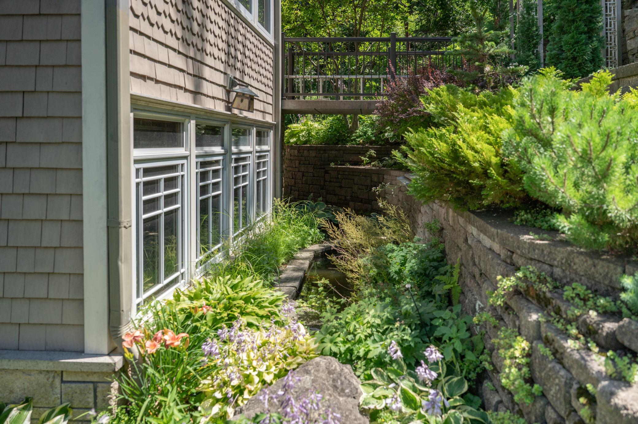 The bank of windows at left sit at the edge of the dining area in the kitchen and a koi pond and waterfall complete the ambiance. At the back of the frame, a bridge from the home to the hillside paths can be seen.