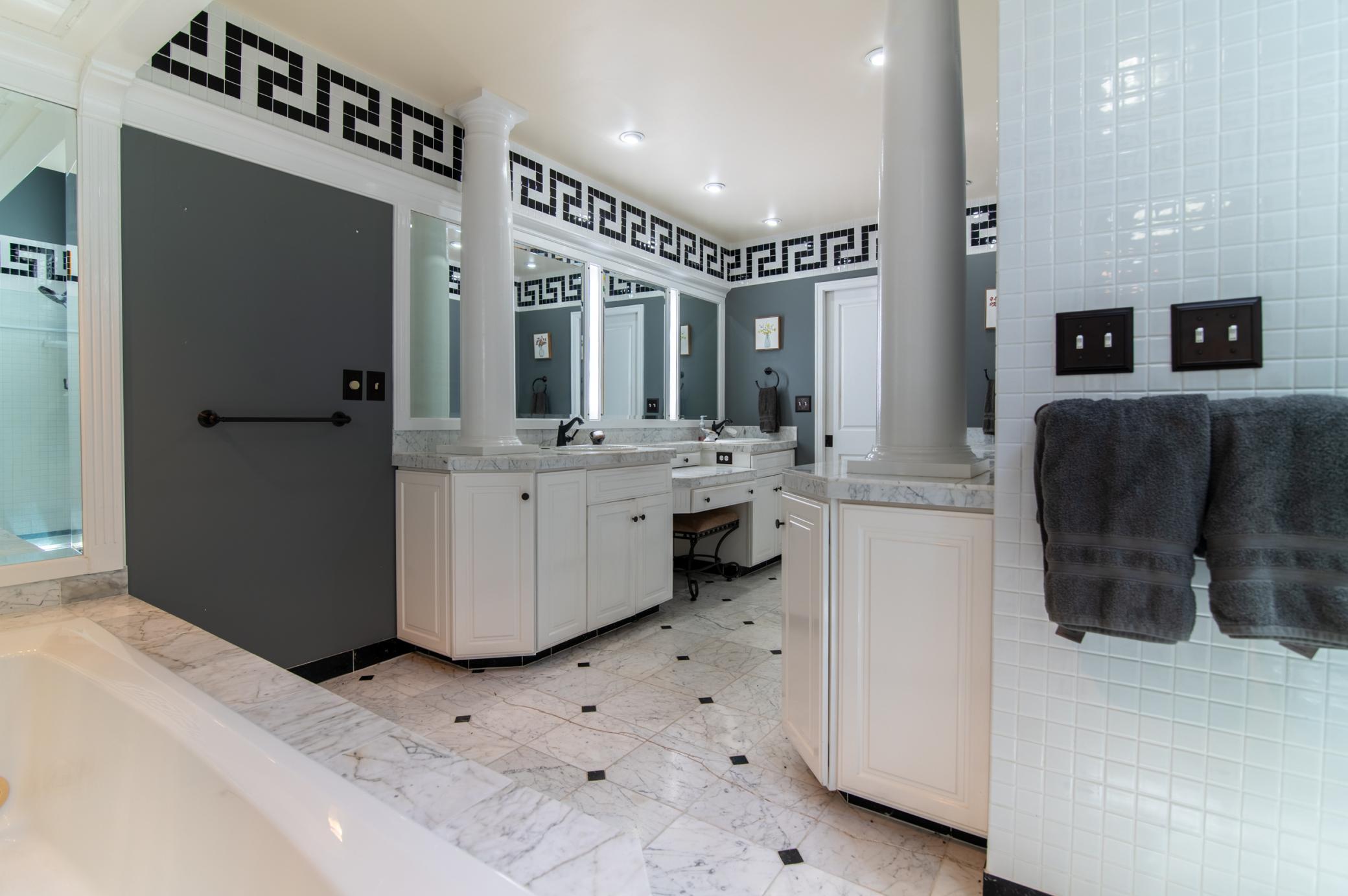 The luxurious main floor full bath sits off the primary bedroom and is complete with white marble finishes and classic Greek key detailing around.