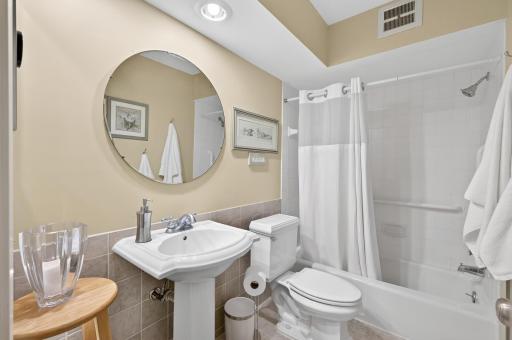 White ceramic tiled bath, has tile flooring and is enhanced by a pedestal sink, updated fixtures and a large linen cabinet.