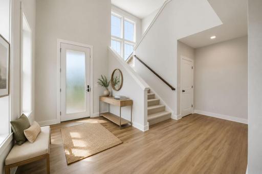 Step into a grand two-story foyer filled with natural light from expansive windows, creating a bright and welcoming first impression. You'll immediately notice the impressive wide staircase, while a discreet door provides access to the lower level.