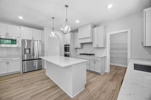 Close-up view of the gourmet kitchen, showcasing quartz countertops, the center island, stainless steel appliances, and the door leading to the expansive 15' x 6' walk-in pantry.