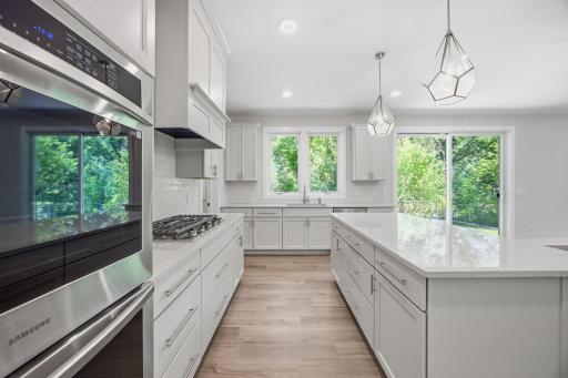 A closer look at the gourmet kitchen, featuring quartz countertops, a center island with abundant storage and shelving, stainless steel appliances, and exceptional design for both everyday living and entertaining.