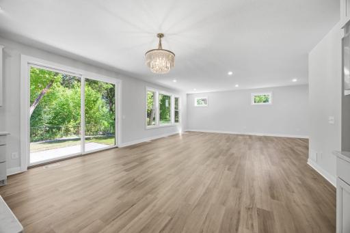 This unfurnished view highlights the open-concept living room and informal dining area, featuring abundant natural light, oversized windows, and a sliding glass door leading to the spacious outdoor patio.