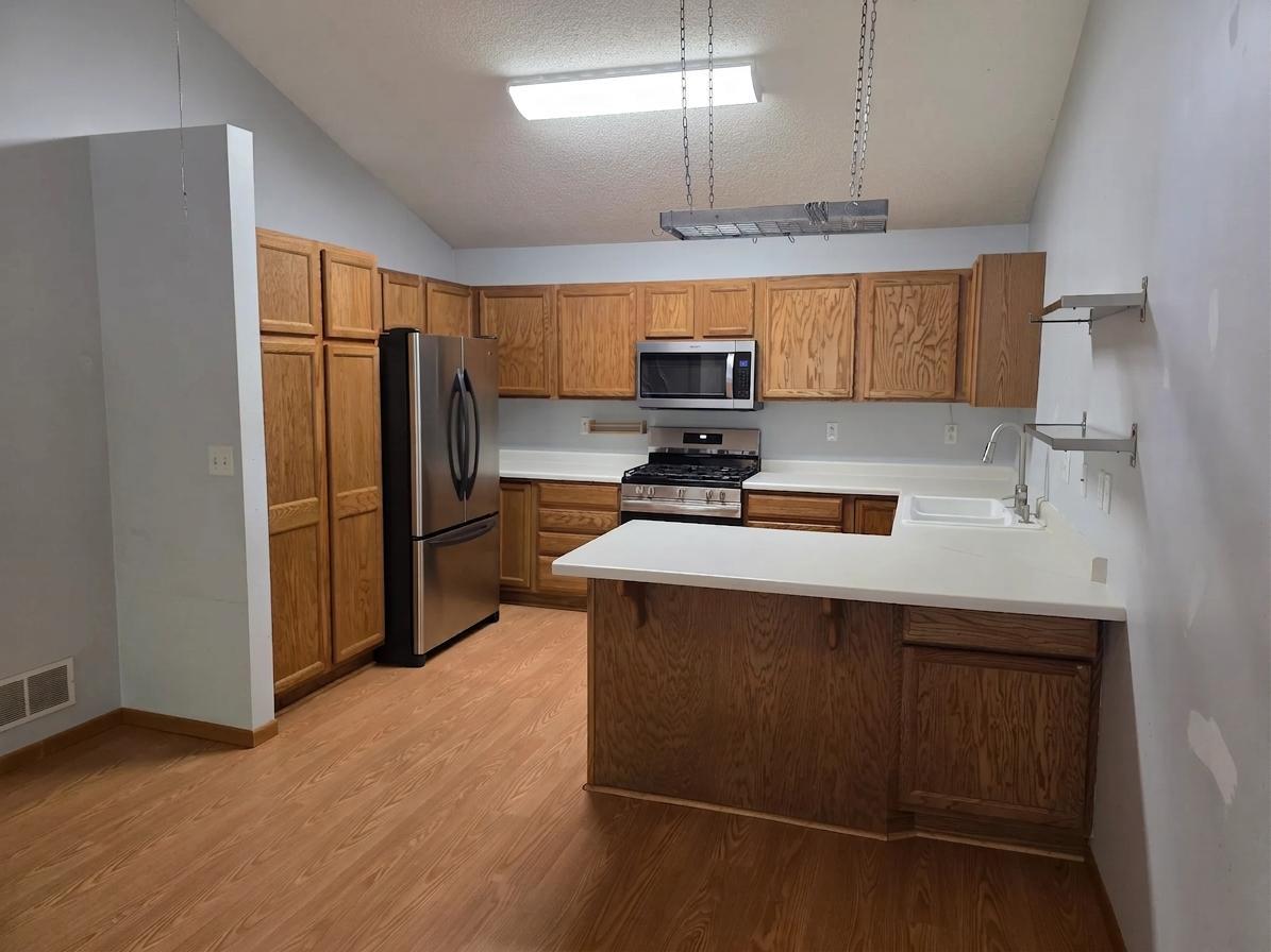 Spacious kitchen with abundant oak cabinetry, expansive countertops, stainless-steel appliances, and a center peninsula.