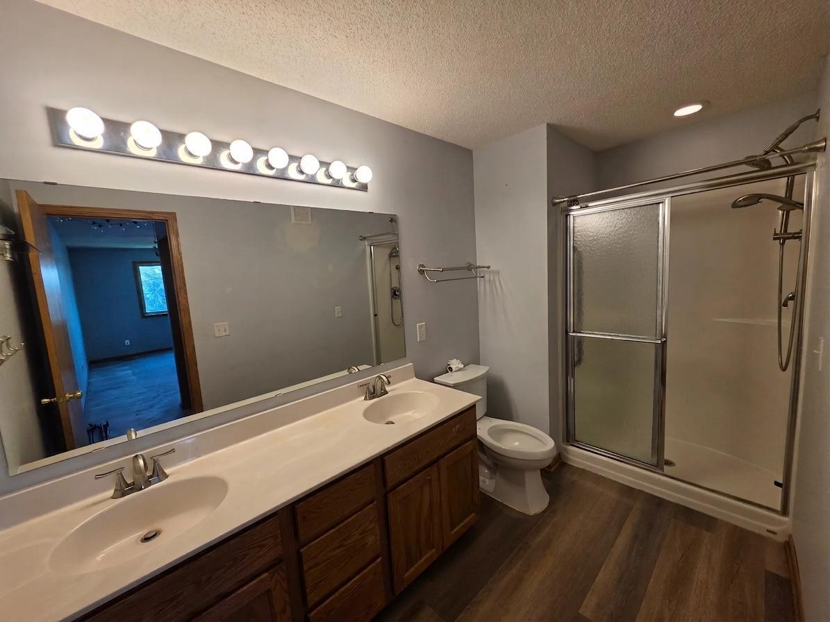 Full bathroom featuring a double vanity, updated flooring, and a separate shower.