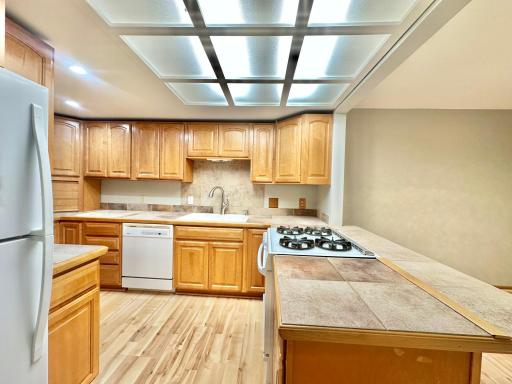 Tile counter tops, laminate wood flooring, gas stove and a tile back splash behind the sink area nicely accessorize the kitchen.