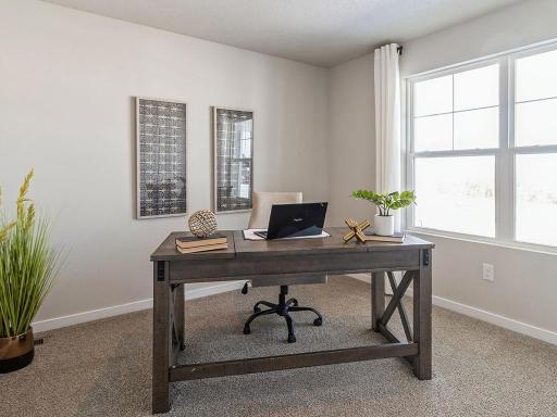 First bedroom staged as an office with large window and desk with chair.